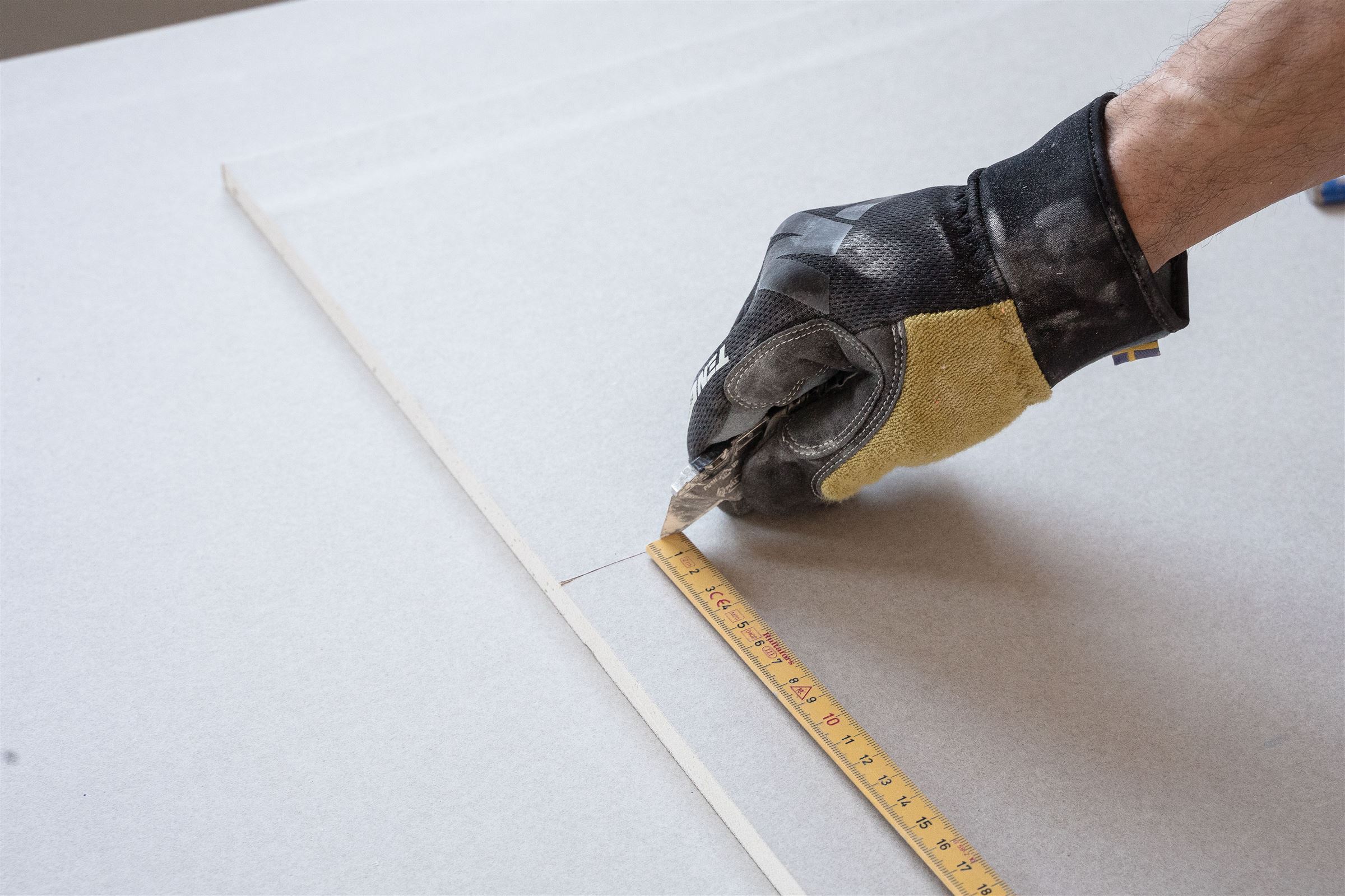 Gipskartonplatte wird mit Messer und Lineal exakt zugeschnitten
